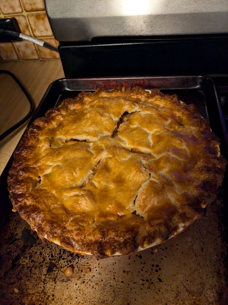 A freshly baked apple pie resting on a half sheet sized tray to contain the drips and spills.