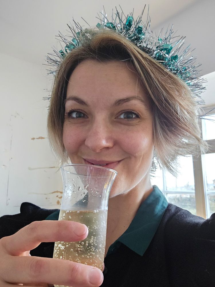 A woman holding a glass of champagne smiles at the camera.