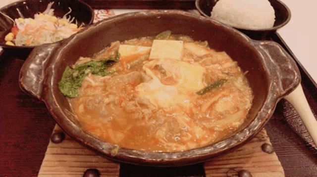 a bowl of stew sits on a wooden stove next to a bowl of rice