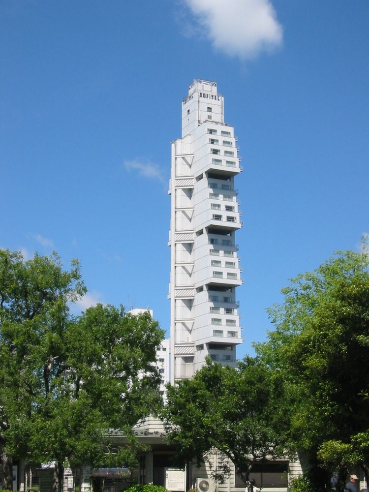 A photo of the Hotel Sofitel Tokyo taken in 2004. The sky is blue with few clouds and the trees framing the unique skyscraper are lush and green, a perfect day. It was demolished in 2007/2008.