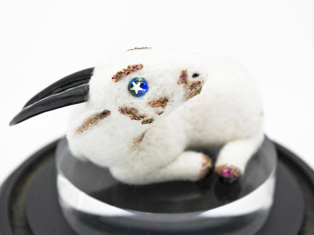 A miniature wool felt sculpture of a Saola - an antelope-like creature with long pointed horns. This Saola is white with starry eyes and glittering markings, but real Saola are brown with white spots.