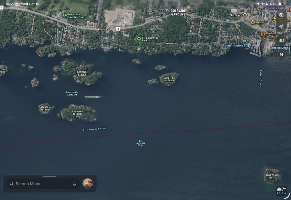 Satellite image of a large river (the St. Lawrence) with a number of small uninhabited islands. On the top right is a marina on the mainland and in the narrows a large cargo ship is heading southwest.