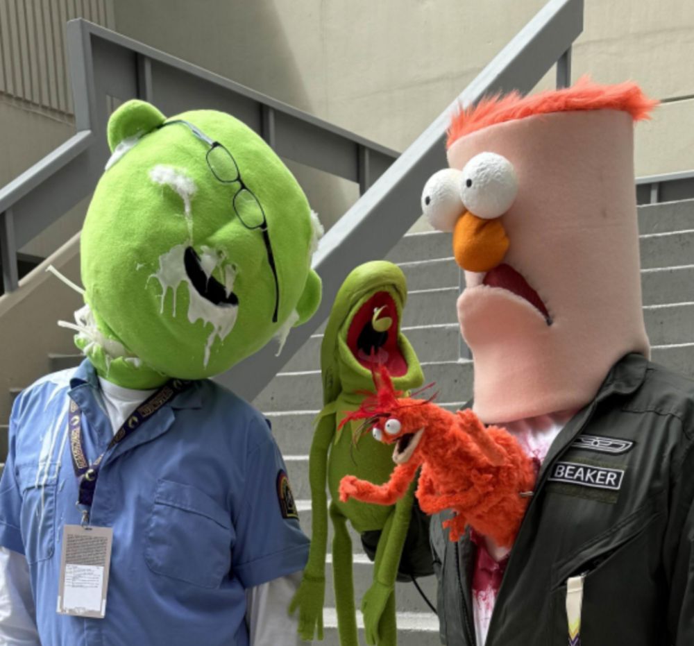 Cosplay of beaker and Bunsen from the Muppets mashed up with alien the movie with a Kermit the frog as the alien and Pepe bursting from beaker's chest.