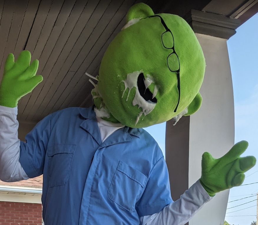 Man in a mashup costume between Ash from the film Alien *blue shortsleeve jumpsuit over longsleeve white t-shirt) and bunsen honeydew (muppe with large green head, green hands)