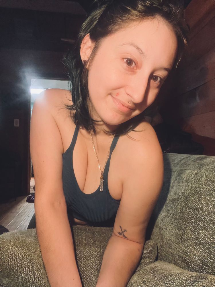 A selfie, glasses on my head, a crystal necklace and a blue fitted tank on, I’m on a green couch