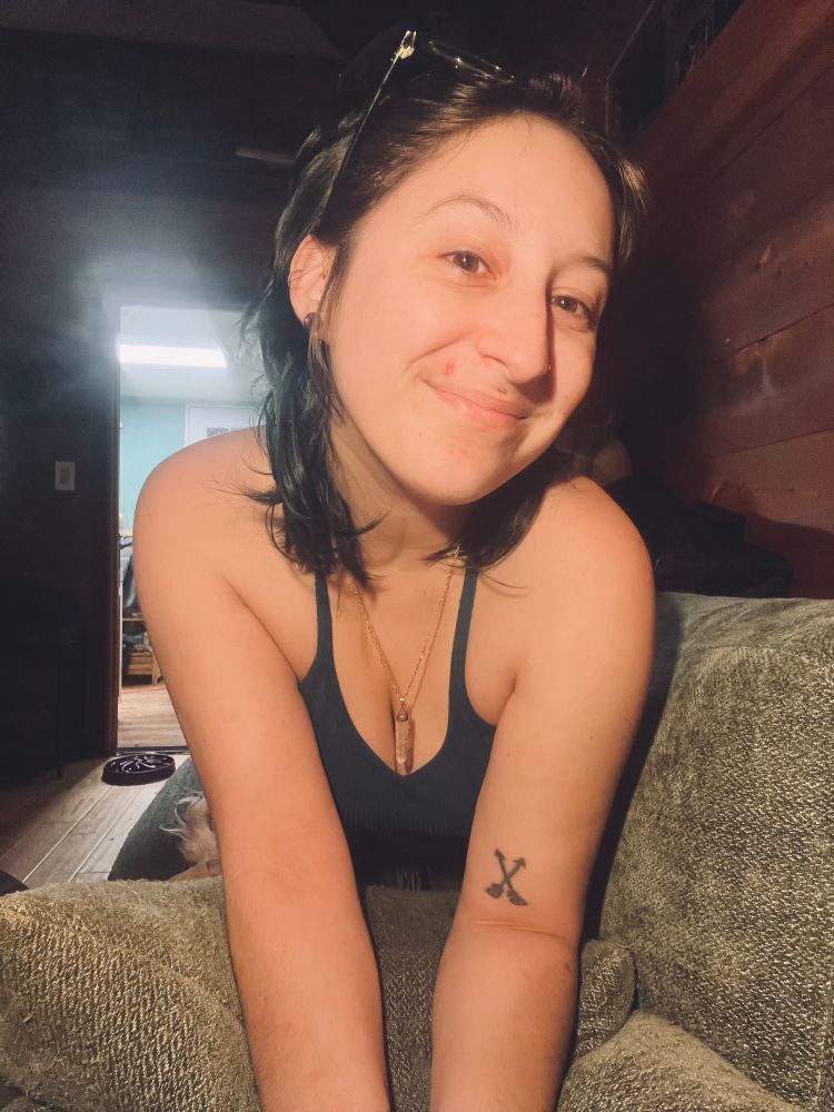 A selfie, glasses on my head, a crystal necklace and a blue fitted tank on, I’m on a green couch