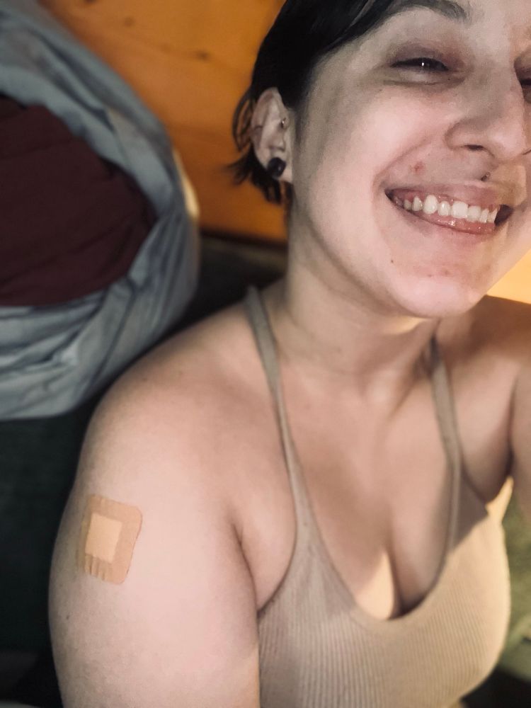 A selfie, I have dark hair tied up, smiling big, a bandaid on my arm