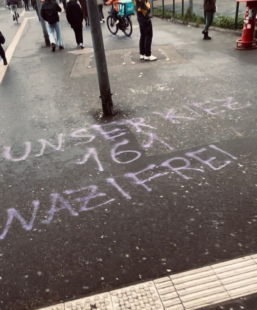 Zu sehen ist der Boden vor dem Bahnhof Ostkreuz, auf dem mit lila Farbe geschrieben wurde: Unser Kiez 161 Nazifrei. 