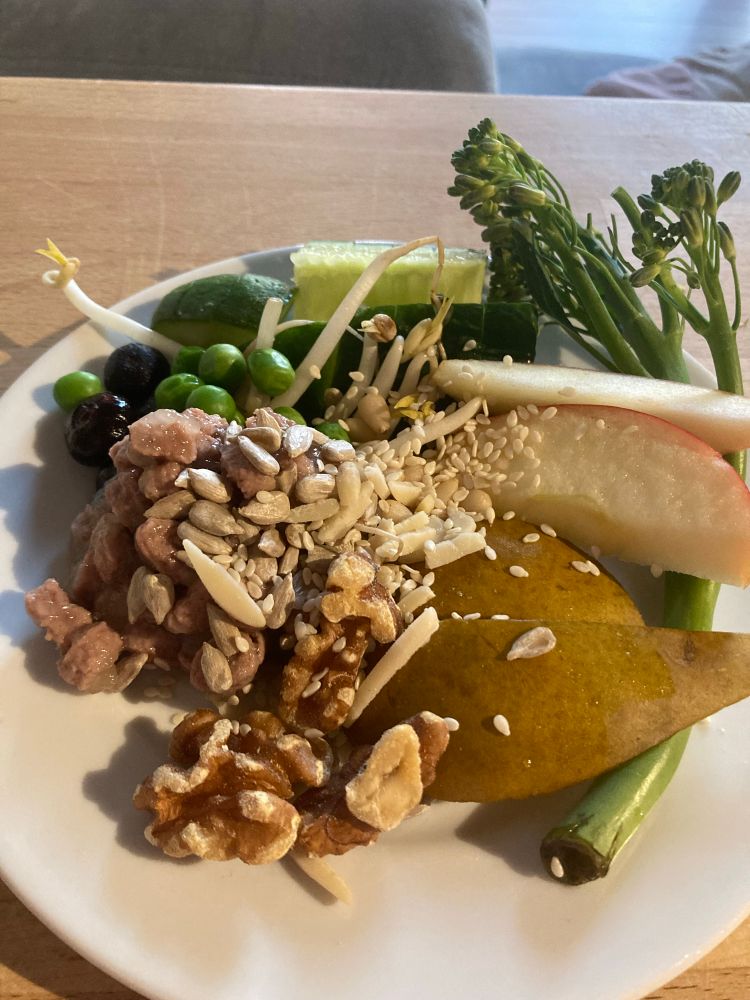 A rat salad with broccolini, sliced apples and peses, peas, blueberries, cucumber, bean sprouts, pine nuts, sunflower kernels, walnuts, sliced almonds, sesame seeds, and wet cat food. 