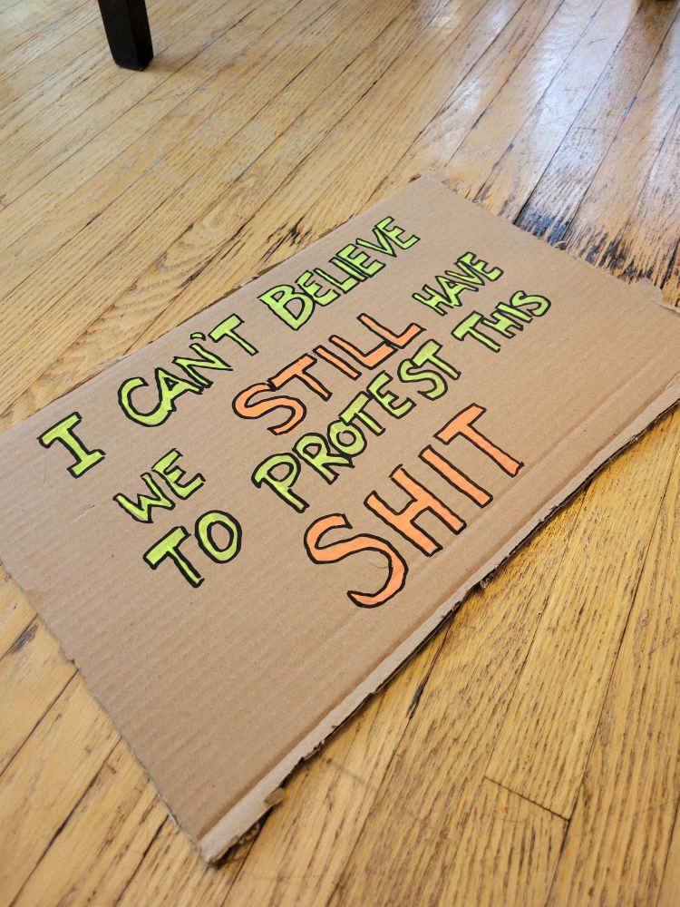 The back of the sign, reading "I can't believe we still have to protest this shit" in neon block capitals