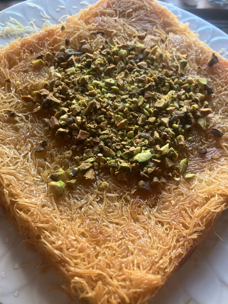whole konafa pastry. golden brown. chopped pistachios on top 
