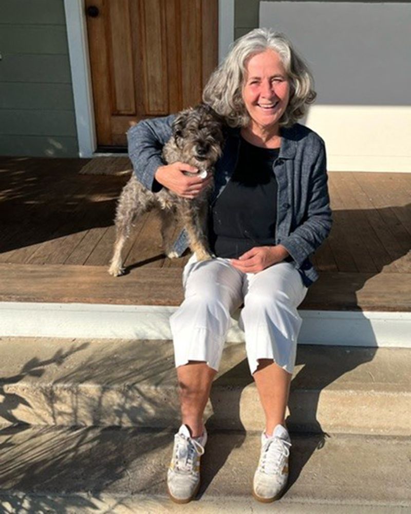 Photograph shows Bekah sat on some steps holding a dog. You can see the wooden door behind her.