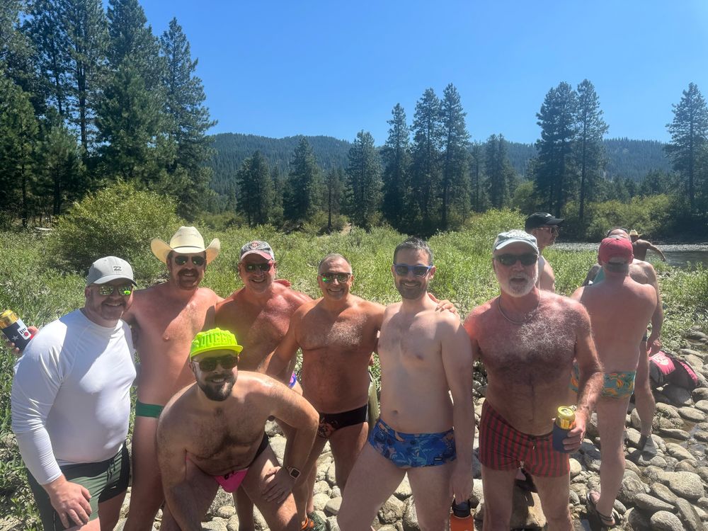 7 men in swimwear pose by the river