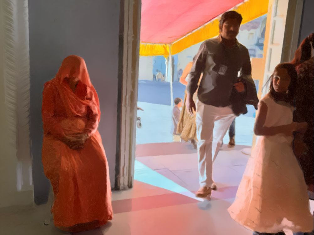 Picture was taken in India at an ancient Muslim fortress. A father follows his young daughter who is wearing a flowing dress through a doorway. To their right is an older woman who is seated and whose head is completely veiled.  Her hands are folded in her lap.