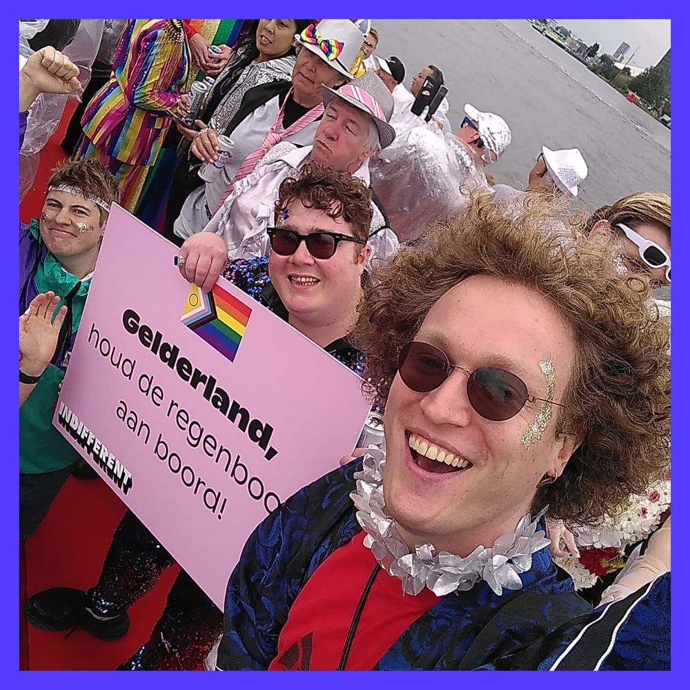 Paul met zonnebril op een boot tijdens de Pride 2023. Achter hem een bord van het COC en Indifferent met daarop de tekst "Gelderland, houd de regenboog aan boord!"