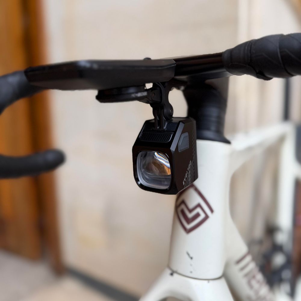 A front view of the bike once the mount is repaired; The image shows the detail of a black gravel handlebar, with a Coros DURA computer cycling, and the Magicshine headlamp 
