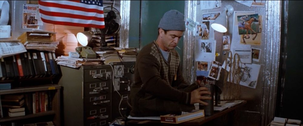 Screen still from the movie "Conspiracy Theory." The character plays a conspiracy theorist who is obsessed with coincidences and obscure occurrences. In this scene, he prepares his desk to skim newspapers and highlight notable headlines.
