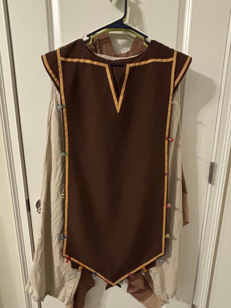 A brown smock with gold trim hanging up against a door.