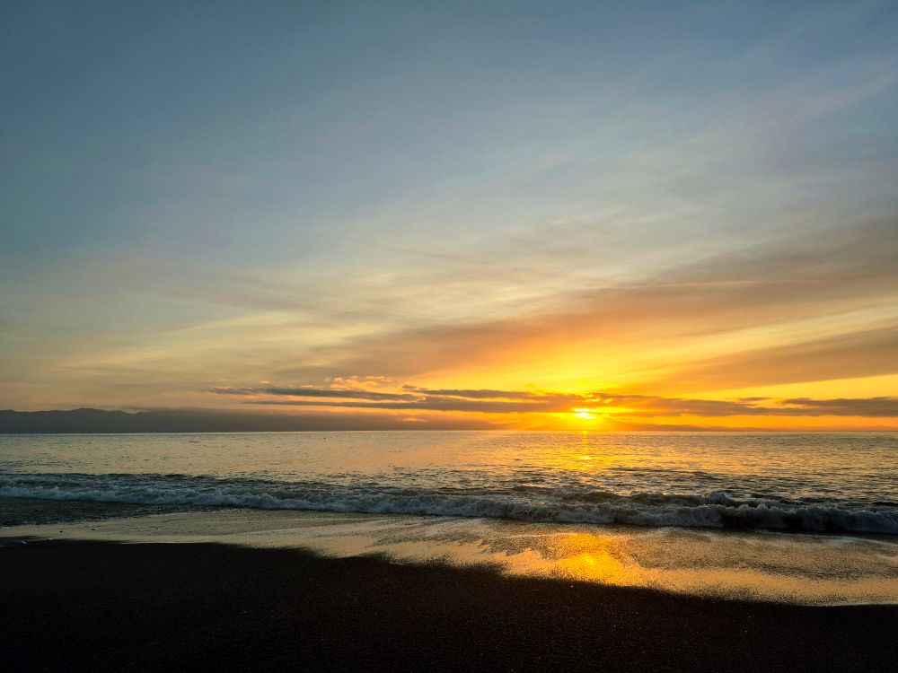 Sunset over the Pacific Ocean, the landscape glows in golden light. 