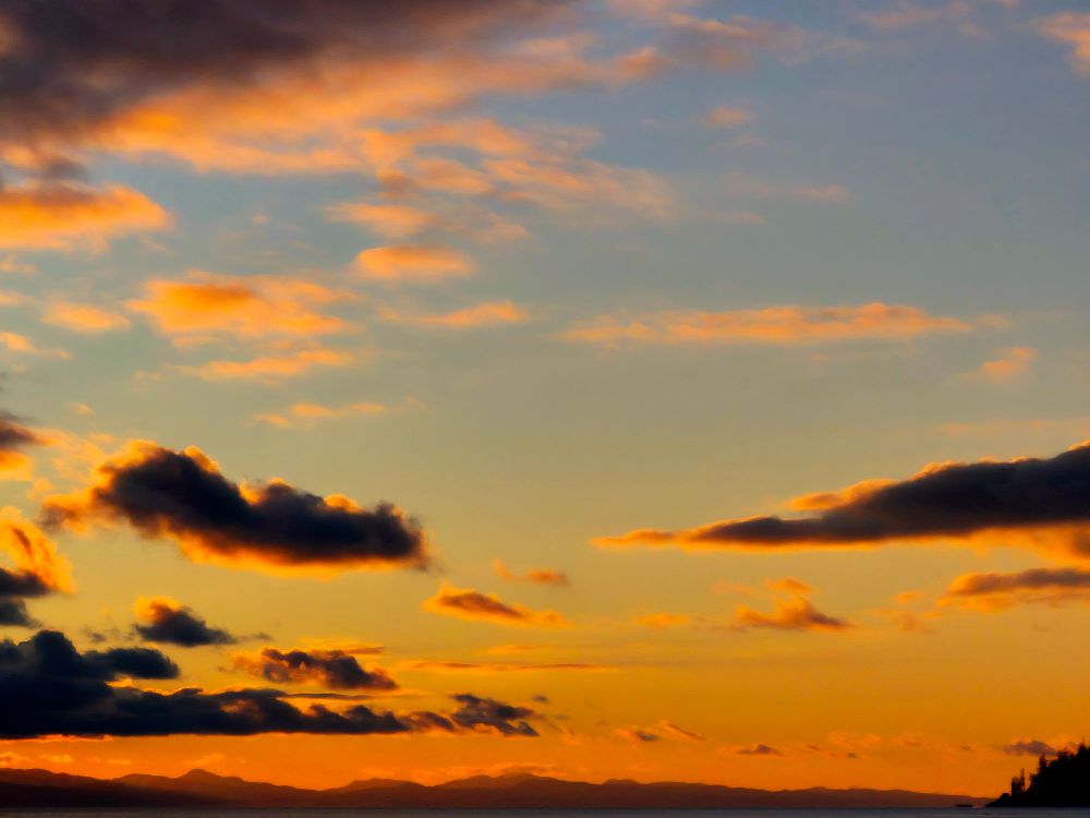 The sun dips low, a final, golden gasp,
Above the mountains in the twilight's hold.
Within this moment, our brief world we clasp,
A quiet story silently untold.
Vast heavens watch our hurried, fragile trace,
Dark clouds are shadows of a passing day.
We are but dust within this endless space,
A flicker in the light that fades away.