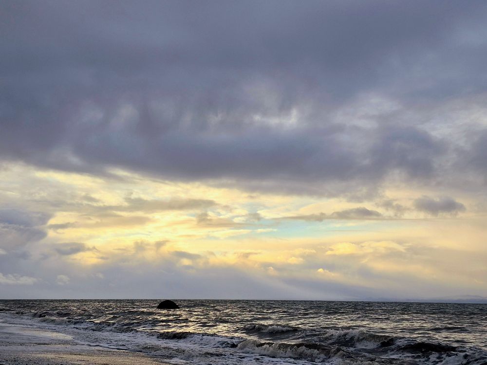 Waves crash to shore on the coast of Vancouver Island. The dense clouds are breaking with sun beams and blue sky shining through. 