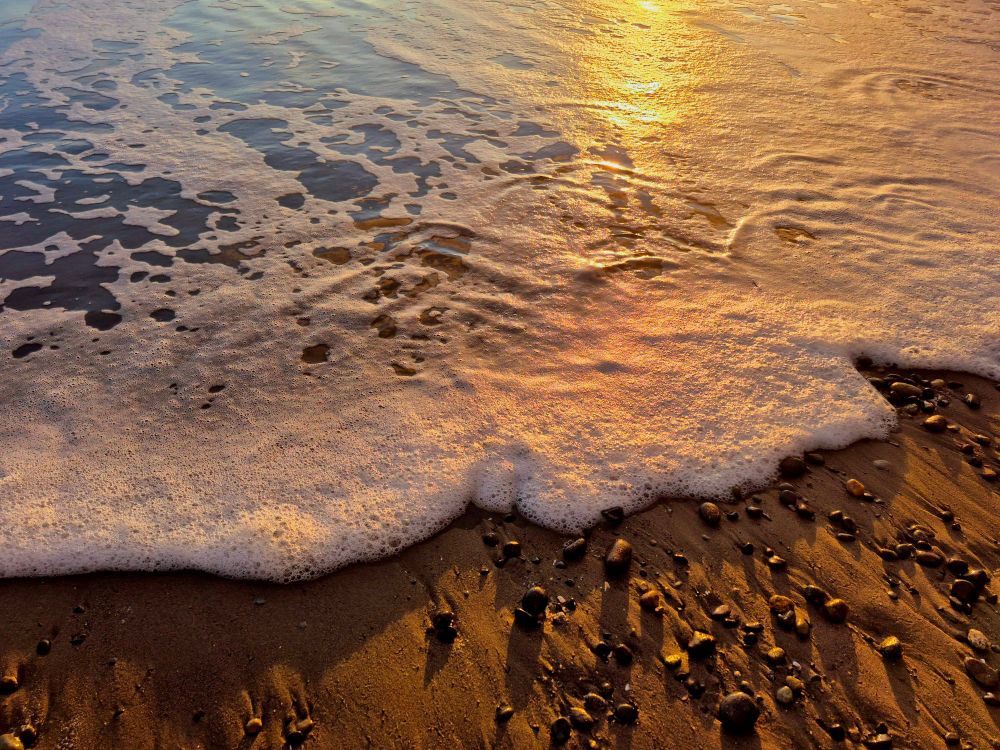 Foamy frills, 
the oceans evening dress, 
ripples of gold, 
shadows on the sand. 

A pillowed caress, 
a seafoam serenade, 
pebbled pearls perched, 
where the sea meets the land. 

Sunset swirls, 
in tangerine hues, 
dreamlike splendor, 
mindful truth. 

The rising tide of fading light, 
a slow and passionate kiss goodnight.