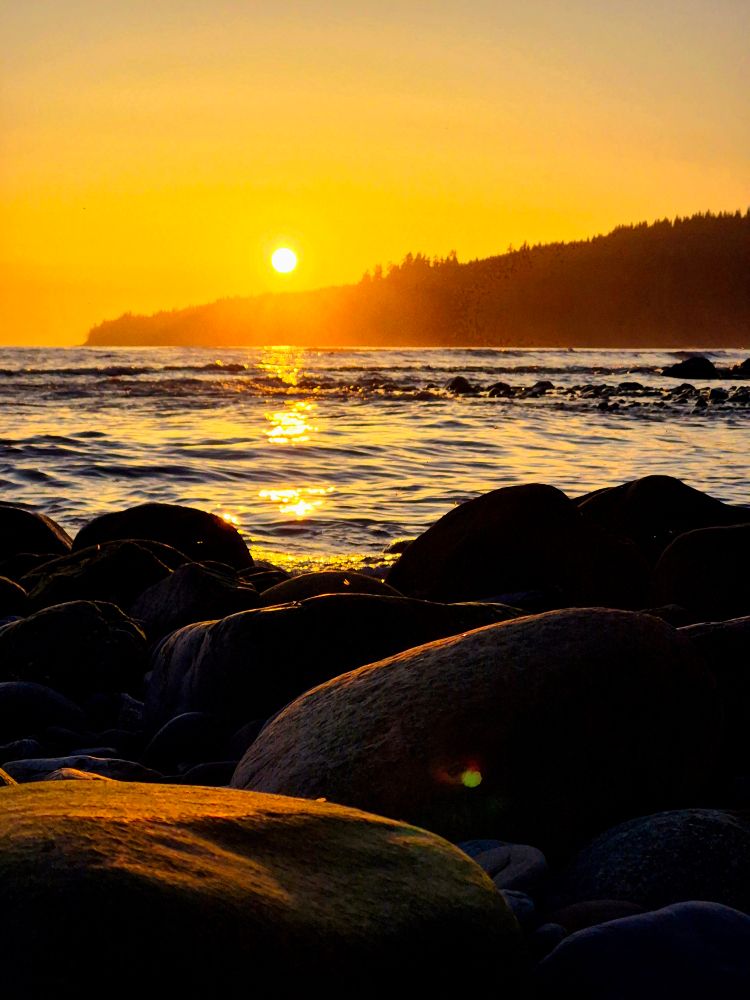 The sun decends toward the horizon, igniting the sky in a blaze of color. Waves of gold rush the shore to greet the glowing stones. A dance they've done a million times, yet they still meet to dance at dusk once more. Serenity seeps slowly, soul soothing sounds serenade the shoreline.