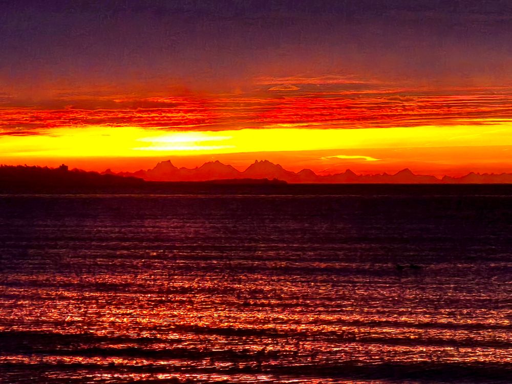The sun is just below the horizon, its light setting the sky on fire. A distant mountain range is silhouetted against the bright red sky.