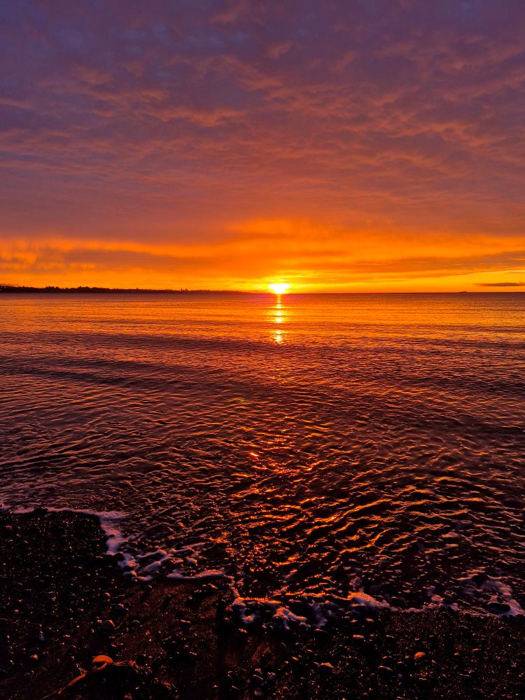 A view of the Pacific Ocean, the sun sits on the horizon illuminating the landscape in beautiful colors.