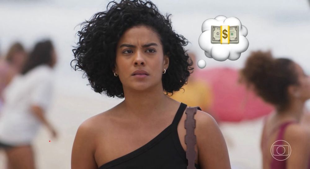 A imagem mostra Maria de Fátima, personagem icônica da novela Vale Tudo, em uma praia. Ela aparece em destaque, com expressão séria e determinada, vestindo uma blusa preta de alça única e carregando uma bolsa no ombro. Ao lado de sua cabeça foi inserida uma ilustração de balão de pensamento com a imagem de maços de dinheiro, reforçando a principal característica da personagem: a ambição desmedida e o desejo incessante de ascender socialmente a qualquer custo. Fátima simboliza a busca por status e riqueza, sempre pronta a manipular ou trair para alcançar seus objetivos, em contraste com valores de ética e solidariedade que a trama questiona. O cenário de praia, com pessoas ao fundo desfocadas, destaca ainda mais seu isolamento emocional e foco no poder e no dinheiro.
