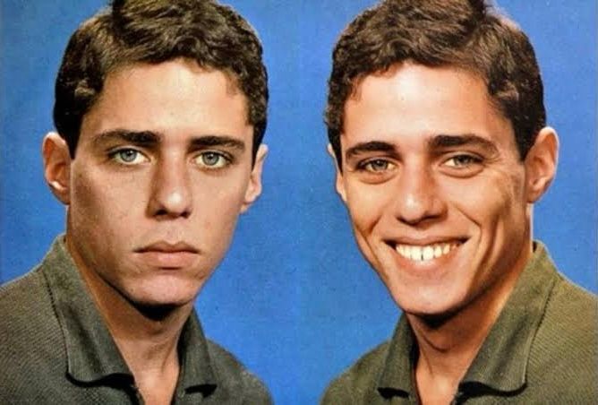 A imagem mostra um homem jovem, retratado duas vezes lado a lado, sobre um fundo azul. À esquerda, ele aparece sério, com expressão neutra, lábios fechados e olhar fixo para a câmera. À direita, o mesmo homem está sorridente, exibindo os dentes e uma expressão de alegria. Ele tem cabelo castanho curto, olhos claros e veste uma camisa de tom esverdeado. A imagem ressalta o contraste entre as duas expressões faciais: uma séria e introspectiva, a outra aberta e simpática.