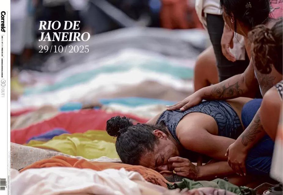 A imagem, datada de 29 de outubro de 2025, mostra uma cena comovente no Rio de Janeiro. No primeiro plano, um homem está prostrado, chorando com o rosto coberto pelas mãos, em meio a lonas e cobertores coloridos estendidos no chão. Ele é consolado por uma mulher que se inclina sobre ele, apoiando a mão em seu ombro, em um gesto de empatia e desespero compartilhado. Ao fundo, outras pessoas aparecem em posição semelhante, criando um ambiente de dor coletiva. A cena transmite um forte sentimento de luto e exaustão, marcada pela vulnerabilidade e pela solidariedade entre os presentes — um retrato intenso da crise humana que atinge comunidades periféricas da cidade.