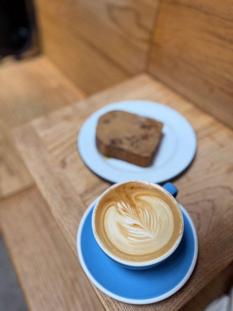 An oat milk cappuccino in a blue cup & saucer with a slice of cinnamon toast on a wood table enjoyed at the Mill on Divisadero Street