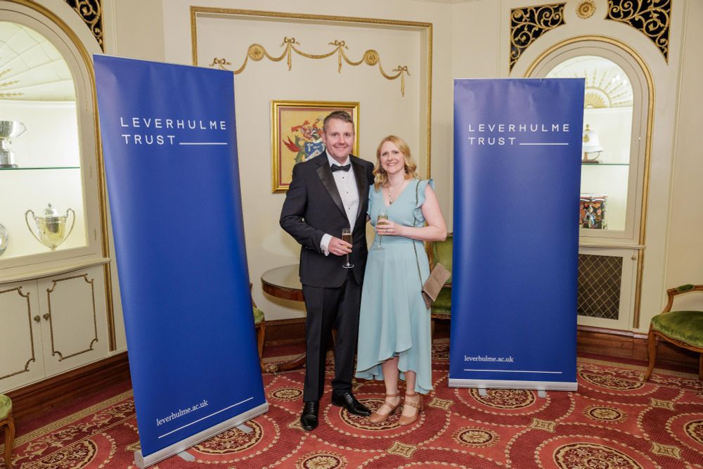 Cathy with her husband dressed smartly and standing in between two Leverhulme Trust banners