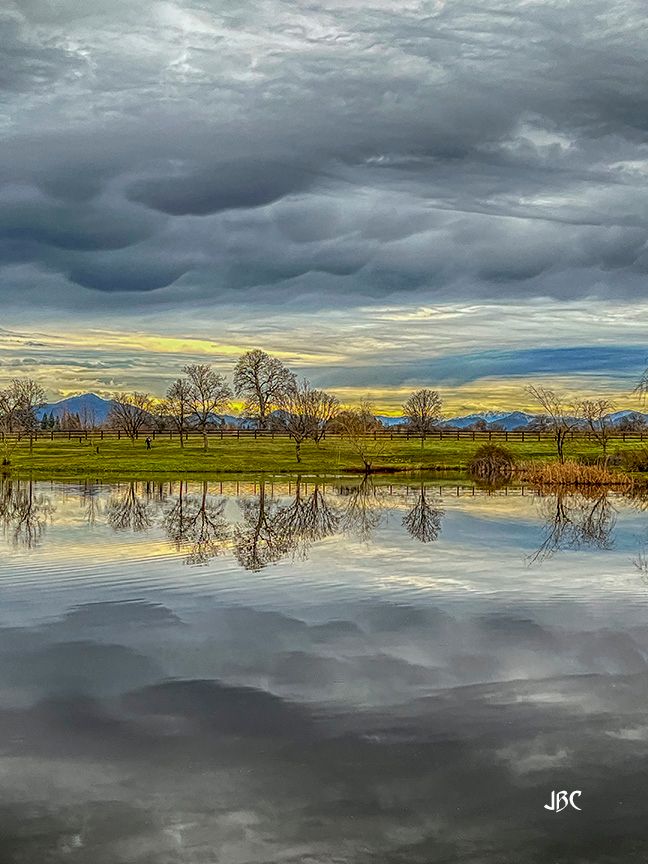mammatus clouds form during sunrise over a pond at Lema Ranch in Redding, CA. Mt Shasta on the left rises above the mountainous horizon