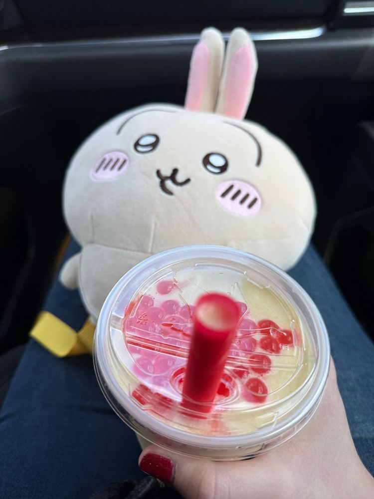 Picture of me holding a Wawa cream mango smoothie with sour cherry popping bubbles in it, and an Usagi Chiikawa plush toy backpack on my lap.