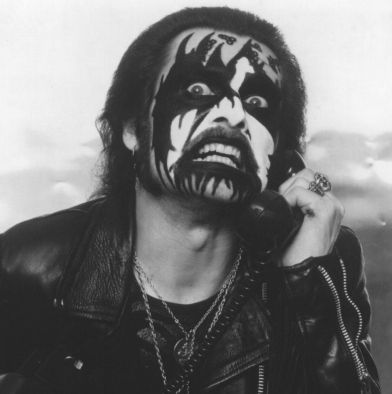 Danish metal singer King Diamond with black and white corpse paint and occult symbols on his face, wearing a leather jacket and holding a phone receiver for some reason. Photo is black and white.