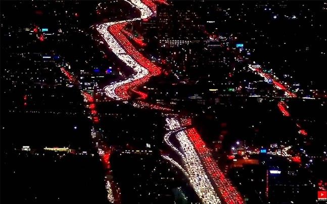 Horrible congestion at night on a Los Angeles freeway at night. A river of congested traffic, some sixteen lanes wide from a drone. The left lanes are all white, the right lanes are all red. No one is getting home anytime soon