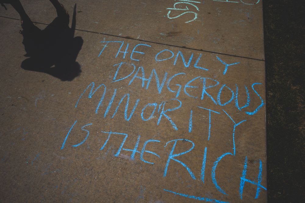 chalk writing on a sidewalk saying THE ONLY DANGEROUS MINORITY IS THE RICH