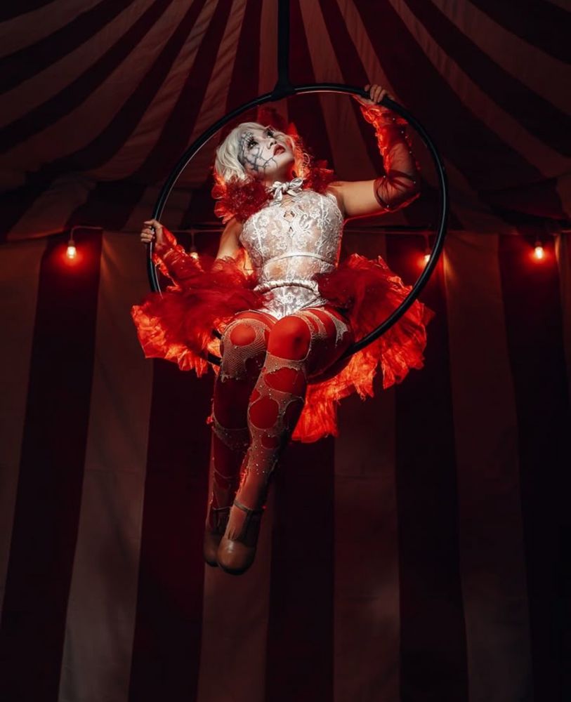 A circus performer in a ref snd white costume hanging onto a flying disk 