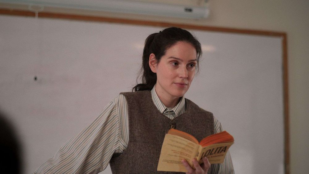 Eva Victor in Sorry, Baby, as an English professor in a sweater vest and reading Lolita