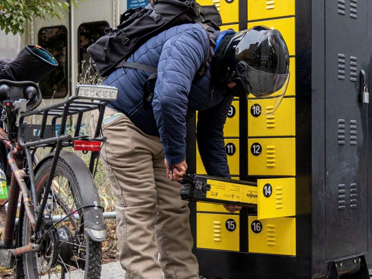 Person wearing bike helmet removes e-bike battery from yellow locker cabinet 
