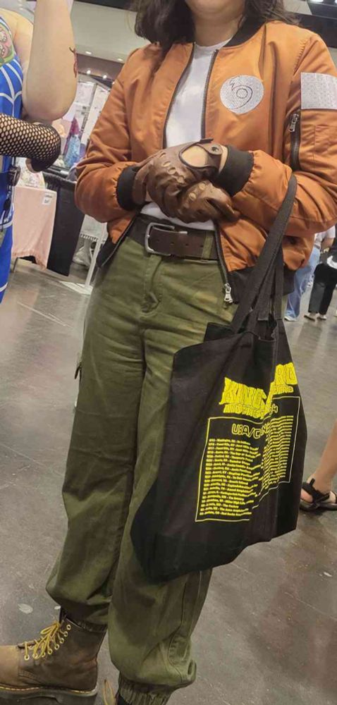 me in cosplay with an orange bomber and green pants with leather boots, gloves, and belt