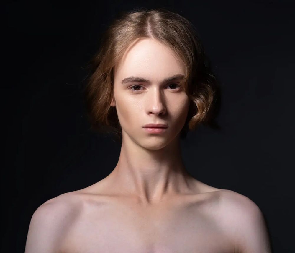 A portrait photograph of a white androgynous person looking directly at the camera.