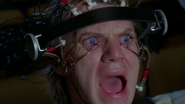 Malcolm McDowell in a scene from A Clockwork Orange, strapped to a chair screaming as his eyes are held open by metal bars and he’s forced to watch violent imagery. 