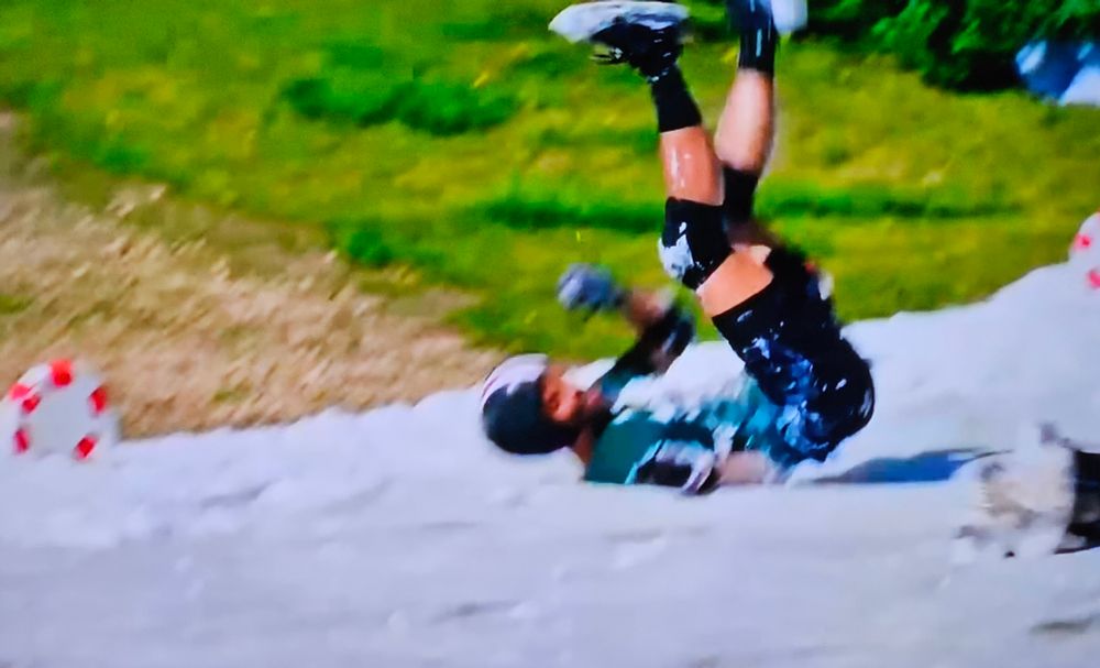 A dude in shorts falling on his back on a white slip and slide. 