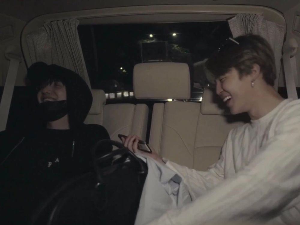 A pic of yoongi and jimin sitting in the back of a car, both are laughing cutely. Yoongi is dressed in black and has a mask over his chin, jimin is dressed in white, he's wearing sunglasses on top of his head and is holding his phone.