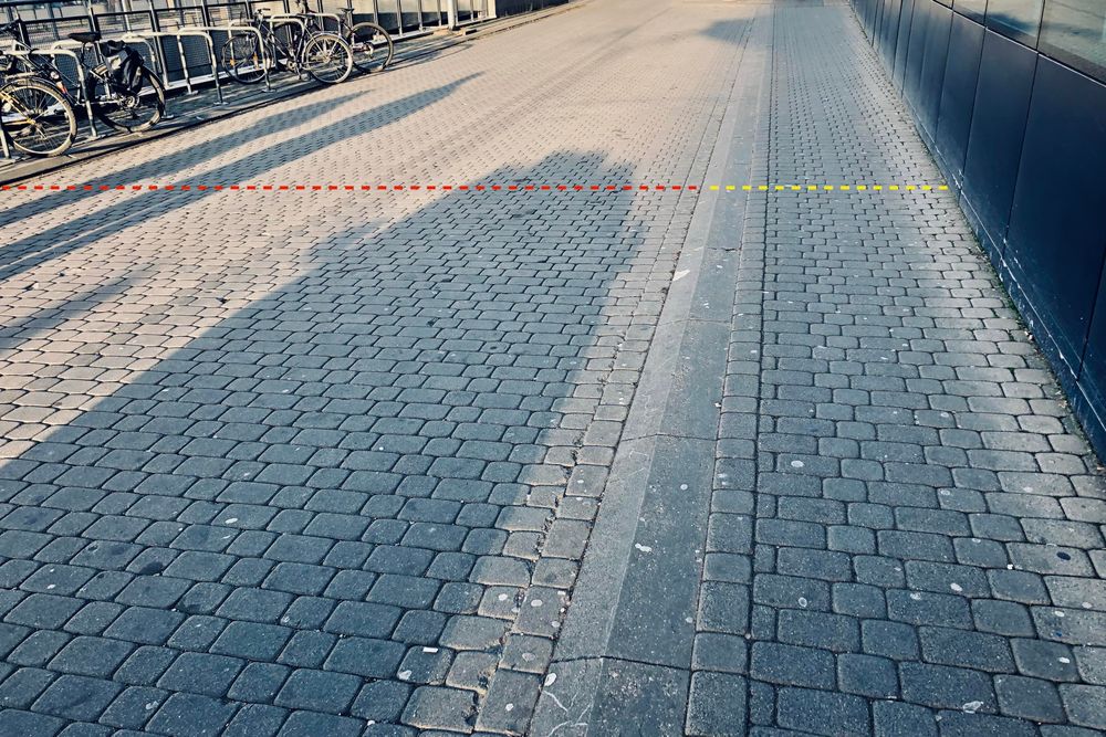 Zdjęcie przedstawia jezdnię z chodnikiem z kostki polbruk przed wejściem do centrum handlowego Blue City w Warszawie. Chodnik ma ok 1.5 metra, jezdnia 5-6 metrów szerokości.