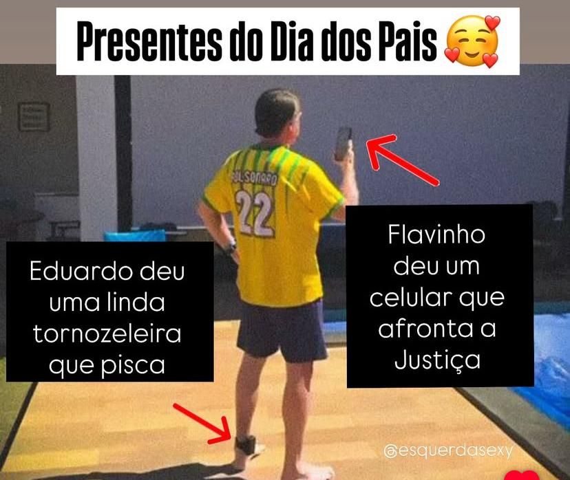 Foto de Bilorido de costas, vestindo uma camisa amarela com "Bolsonaro 22" escrito. Ele está usando uma tornozeleira eletrônica no pé e segurando um celular. Há duas caixas de texto irônicas na imagem. A da esquerda diz: "Eduardo deu uma linda tornozeleira que pisca". A da direita diz: "Flavinho deu um celular que afronta a Justiça". No topo está escrito: "Presentes do Dia dos Pais 🥰".