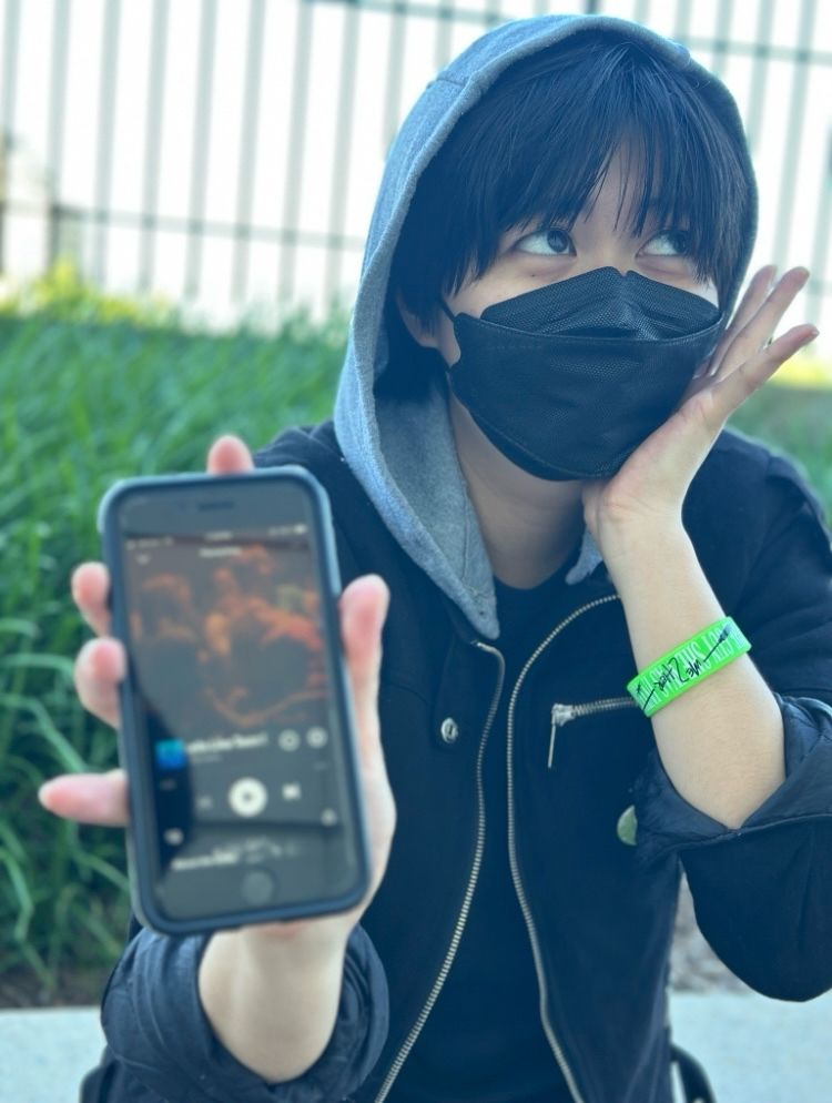 photo of a Mitsuki Koga cosplayer holding up a phone playing “Smells Like Teen Spirit” on Spotify. She holds a hand up to her face and looks off into the distance adoringly